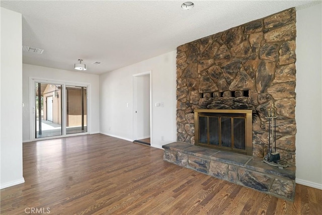 unfurnished living room featuring baseboards, wood finished floors, visible vents, and a stone fireplace