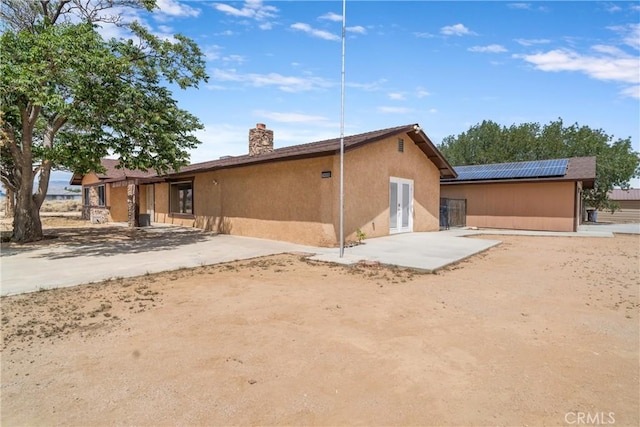 rear view of property featuring stucco siding, a chimney, and solar panels