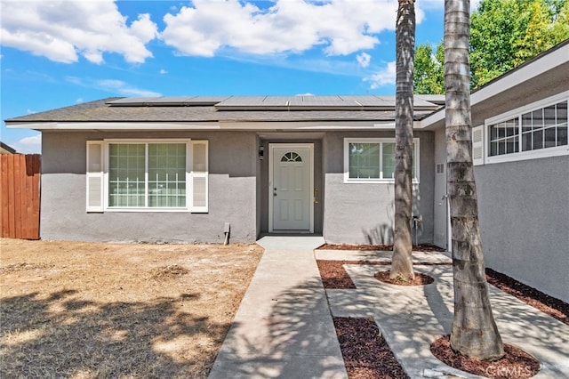 view of front of house with stucco siding, roof mounted solar panels, fence, and a shingled roof