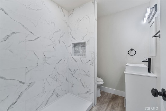 full bathroom featuring vanity, a shower, toilet, wood finished floors, and baseboards