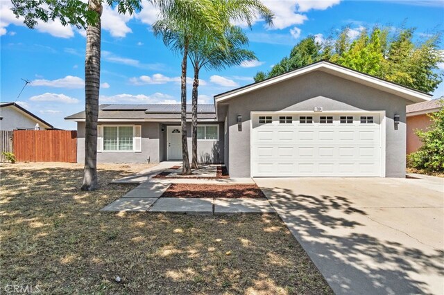 single story home featuring stucco siding, fence, driveway, roof mounted solar panels, and a garage