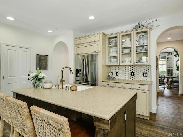 kitchen with stainless steel fridge, arched walkways, a sink, and cream cabinets