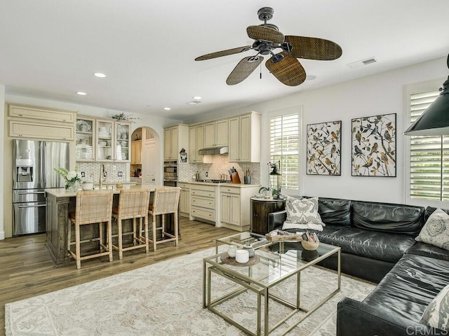 living area featuring visible vents, ceiling fan, recessed lighting, arched walkways, and light wood-style flooring