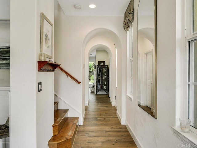 hall with stairway, arched walkways, baseboards, and wood finished floors