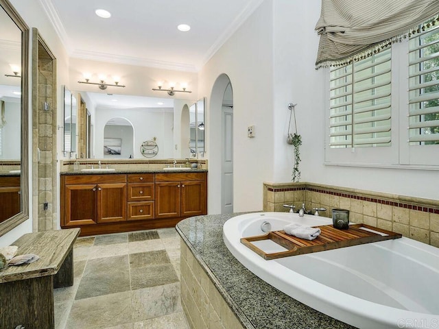 full bath with double vanity, a garden tub, crown molding, a sink, and stone tile floors
