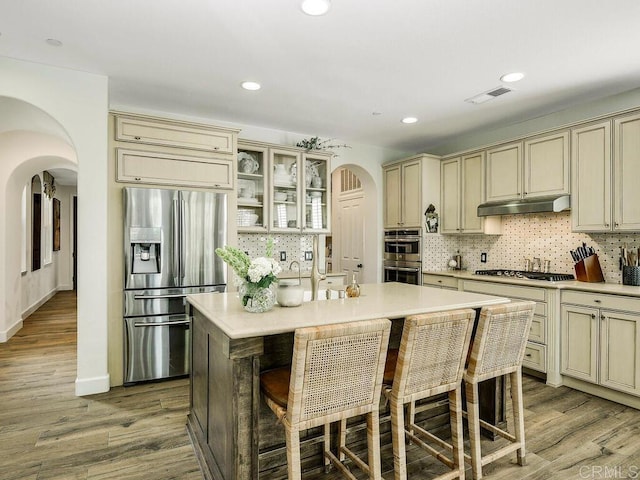 kitchen featuring appliances with stainless steel finishes, arched walkways, cream cabinetry, under cabinet range hood, and visible vents