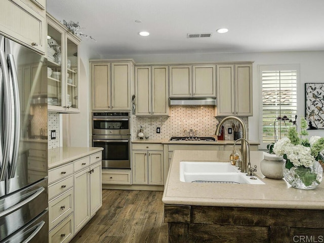 kitchen with dark wood finished floors, stainless steel appliances, cream cabinetry, under cabinet range hood, and visible vents