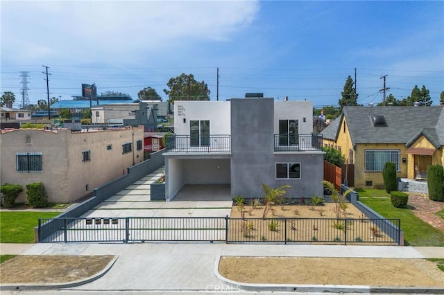contemporary home with driveway, a fenced front yard, a balcony, and stucco siding