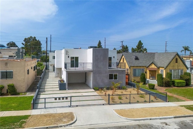 view of front facade featuring a fenced front yard, a gate, a balcony, concrete driveway, and stucco siding