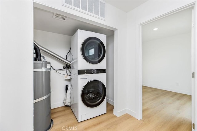 washroom featuring laundry area, stacked washer / dryer, visible vents, strapped water heater, and wood finished floors