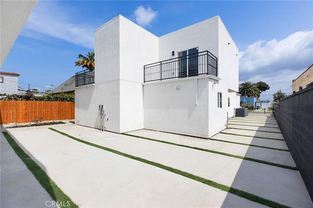 rear view of house with fence, stucco siding, a patio area, and a balcony