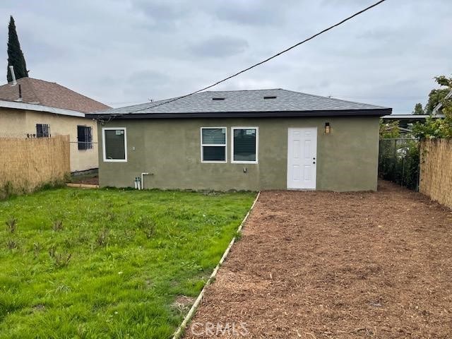 back of house with fence, stucco siding, a yard, and roof with shingles
