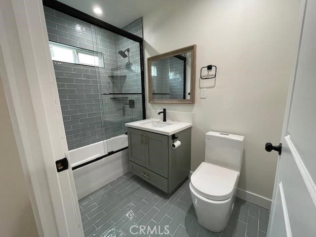 bathroom featuring tile patterned flooring, vanity, baseboards, combined bath / shower with glass door, and toilet