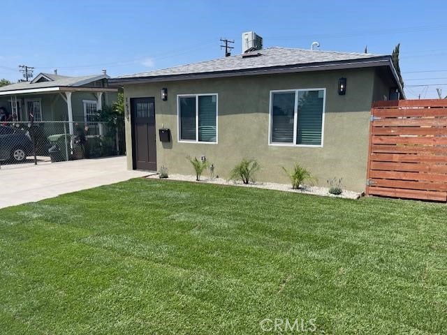view of front facade featuring fence, roof with shingles, stucco siding, a front yard, and central AC unit