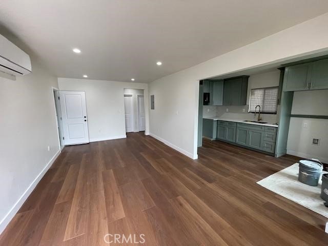 unfurnished living room featuring a sink, an AC wall unit, recessed lighting, baseboards, and dark wood-style floors