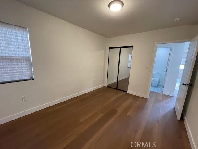 unfurnished bedroom with baseboards, dark wood-style floors, and a closet
