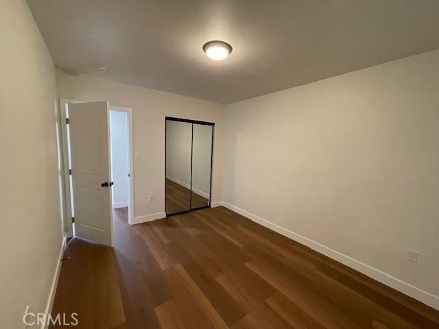 unfurnished bedroom featuring baseboards, dark wood finished floors, and a closet