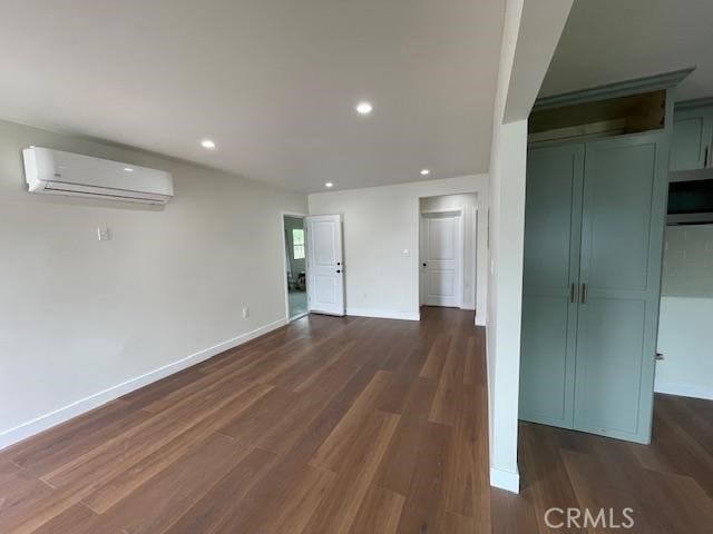unfurnished living room with baseboards, a wall mounted air conditioner, and dark wood-type flooring