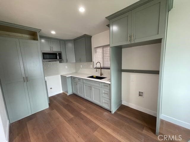 kitchen featuring decorative backsplash, baseboards, dark wood-type flooring, stainless steel microwave, and a sink