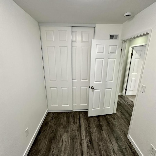 unfurnished bedroom with visible vents, baseboards, dark wood-style floors, and a closet