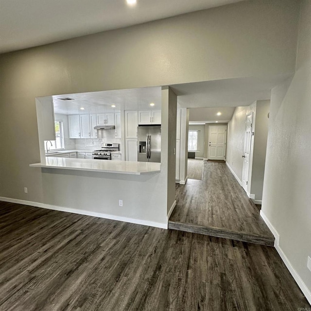 kitchen featuring stainless steel appliances, light countertops, under cabinet range hood, white cabinetry, and dark wood-type flooring