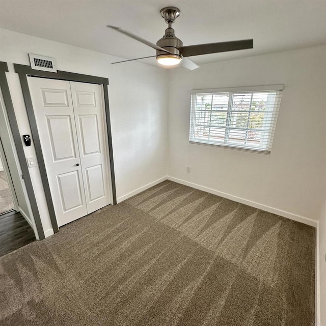 unfurnished bedroom with dark colored carpet, a ceiling fan, baseboards, visible vents, and a closet