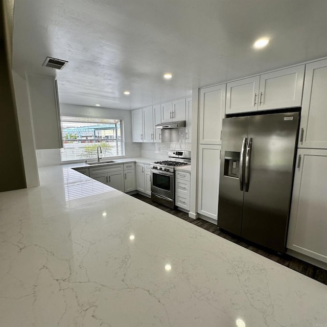 kitchen featuring visible vents, light stone countertops, under cabinet range hood, a sink, and appliances with stainless steel finishes