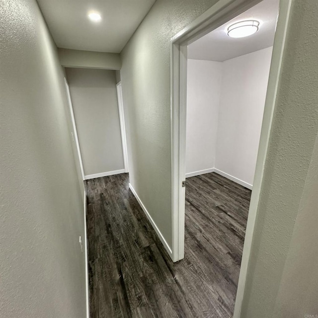 corridor featuring baseboards, a textured wall, and wood finished floors