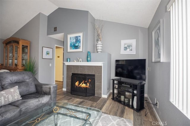 living room with visible vents, vaulted ceiling, wood finished floors, and a tile fireplace