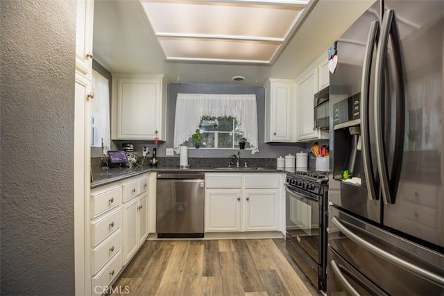 kitchen with dark countertops, a sink, white cabinetry, wood finished floors, and black appliances