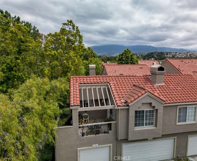view of front of home featuring a tile roof, a garage, stucco siding, a chimney, and a balcony