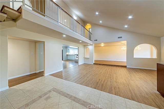unfurnished living room with wood finished floors, baseboards, high vaulted ceiling, a notable chandelier, and recessed lighting