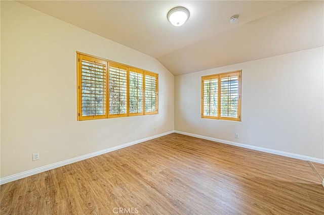 empty room featuring baseboards, vaulted ceiling, a wealth of natural light, and wood finished floors
