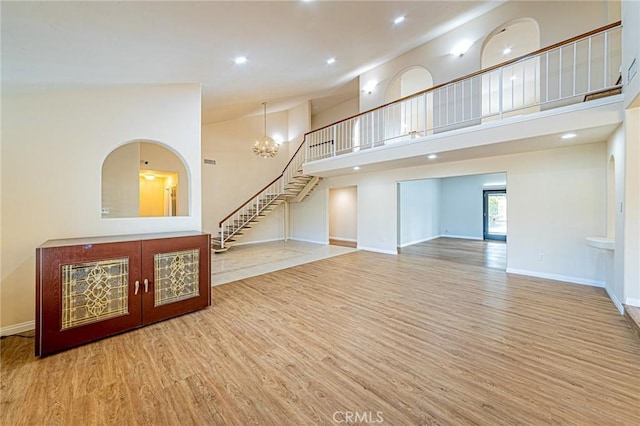 unfurnished living room featuring a high ceiling, recessed lighting, baseboards, wood finished floors, and stairway
