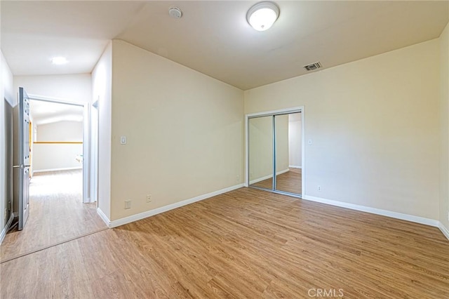unfurnished bedroom featuring visible vents, baseboards, light wood-style flooring, and lofted ceiling