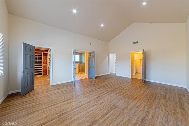 unfurnished bedroom with visible vents, light wood-type flooring, high vaulted ceiling, baseboards, and a spacious closet
