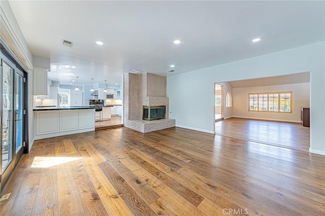 unfurnished living room with wood-type flooring, baseboards, visible vents, and a brick fireplace