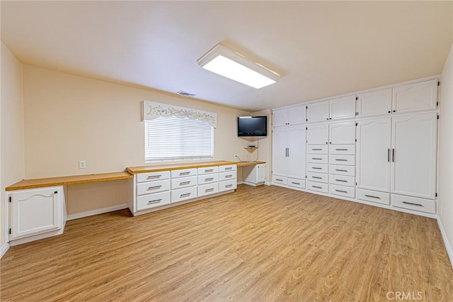 interior space featuring light wood-type flooring, baseboards, built in desk, and visible vents