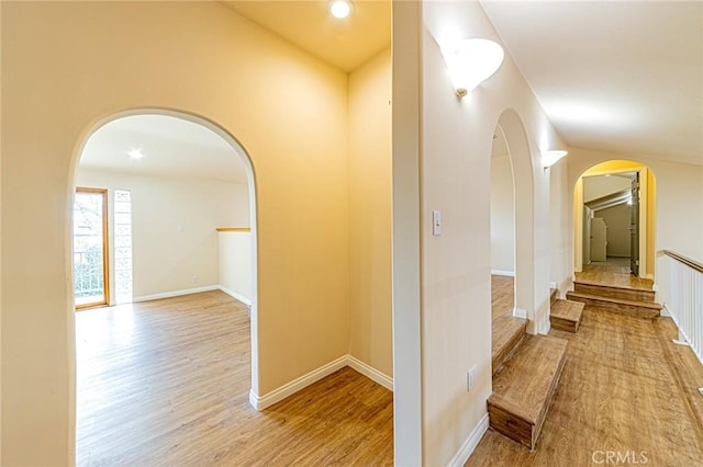 corridor with arched walkways, baseboards, and wood finished floors