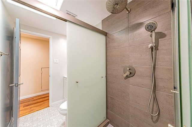 full bathroom with baseboards, toilet, tiled shower, and visible vents