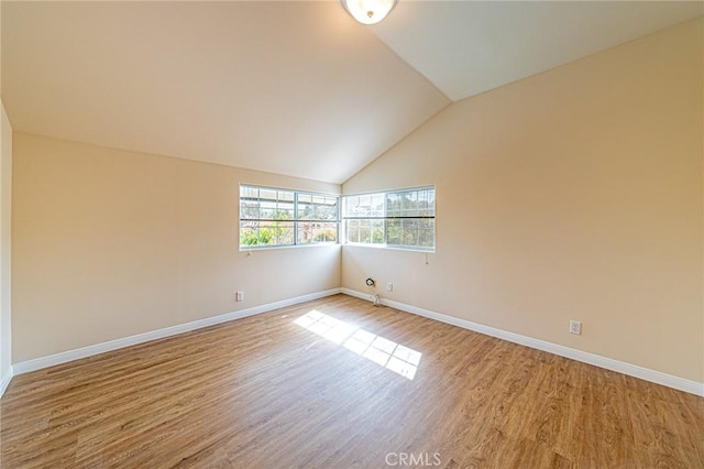 unfurnished room with light wood-style floors, baseboards, and vaulted ceiling