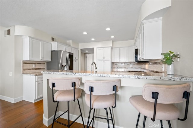 kitchen with stainless steel refrigerator with ice dispenser, visible vents, decorative backsplash, and a peninsula