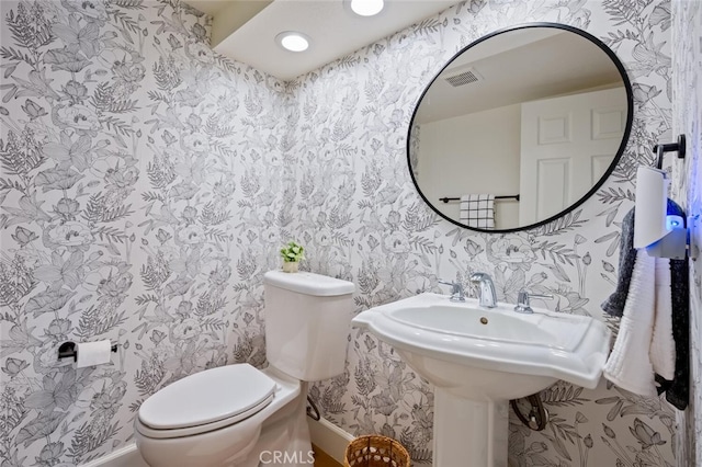 bathroom with toilet, wallpapered walls, visible vents, and baseboards