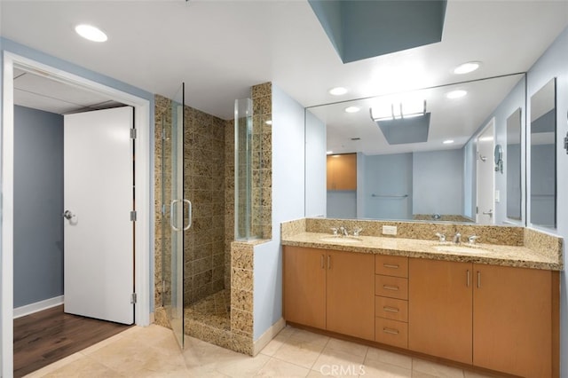 bathroom featuring double vanity, baseboards, a sink, and a stall shower