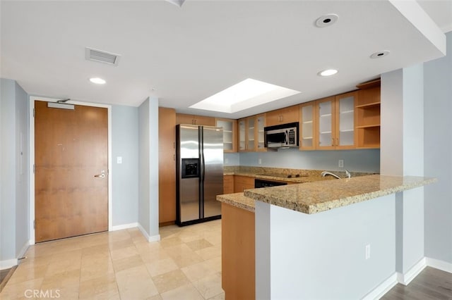 kitchen with appliances with stainless steel finishes, brown cabinets, a peninsula, and visible vents