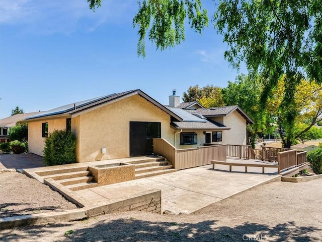 ranch-style home featuring stucco siding, a wooden deck, solar panels, and a chimney