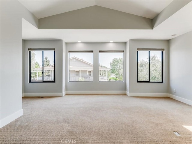 spare room featuring baseboards, light carpet, vaulted ceiling, and a wealth of natural light