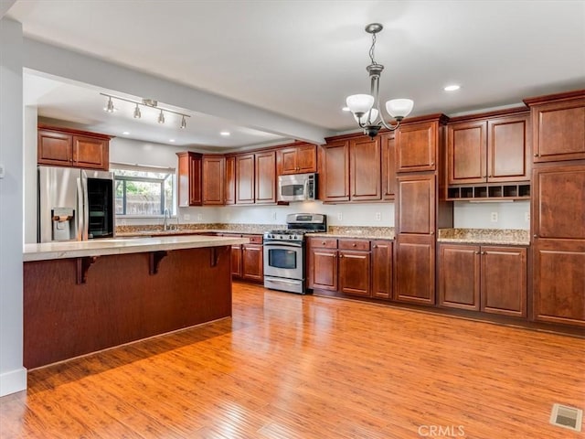 kitchen featuring an inviting chandelier, light wood finished floors, a kitchen breakfast bar, stainless steel appliances, and visible vents