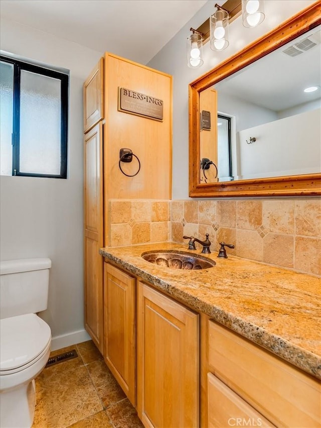 half bath featuring backsplash, visible vents, vanity, baseboards, and toilet
