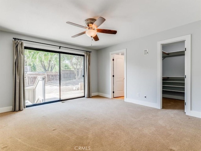 unfurnished bedroom with a ceiling fan, light colored carpet, baseboards, a spacious closet, and access to outside